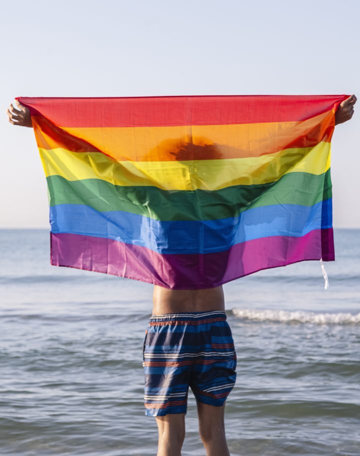 Young latino man raising a lgtbi flag on the beach